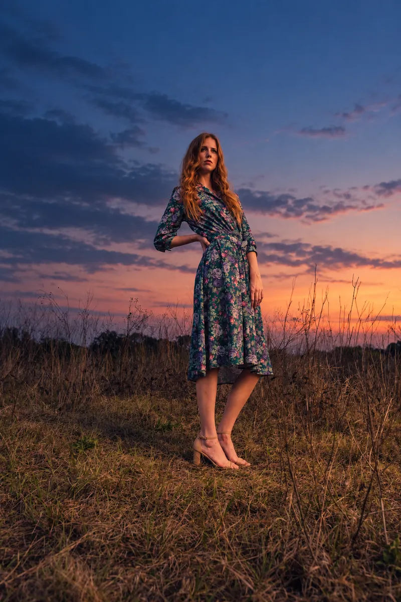 A woman in a floral dress in a meadow under a twilight sky