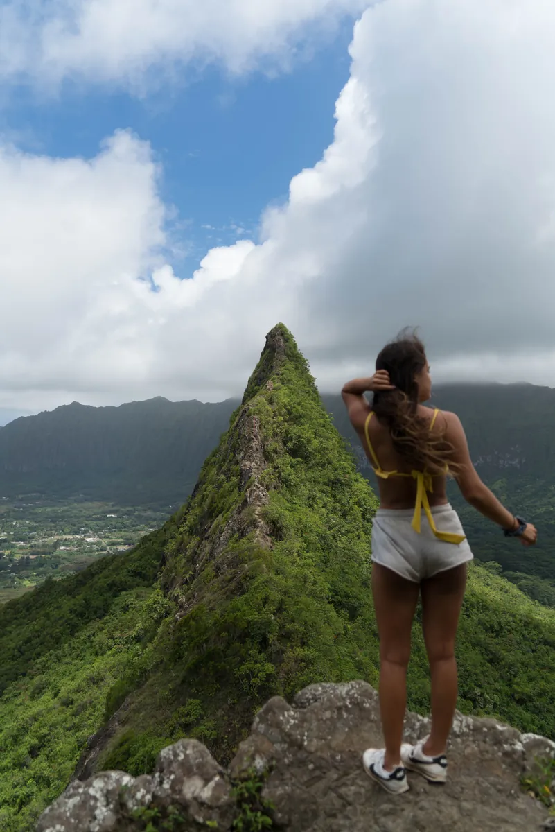 A hiker on a green summit under a flat afternoon sky